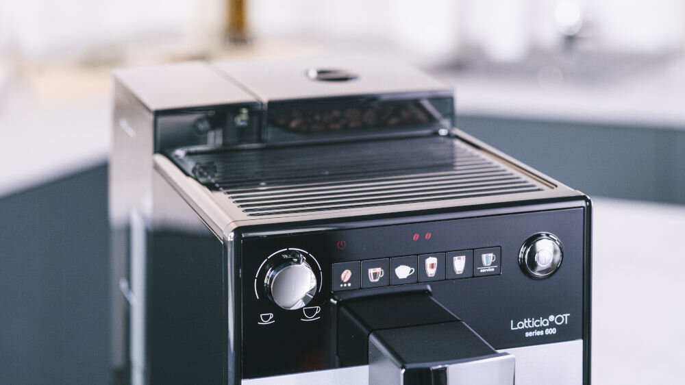 Ekspres do kawy z panelem sterowania zawierającym pokrętło i przyciski z ikonami filiżanek. Na obudowie widoczny jest napis \'Latticia OT series 600\'.