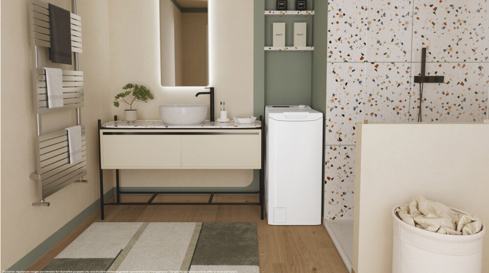 W łazience znajduje się pralka o białej obudowie, obok umywalki na blacie z lustrem. Na ścianie widoczny jest kolorowy wzór, a na podłodze leży dywanik.