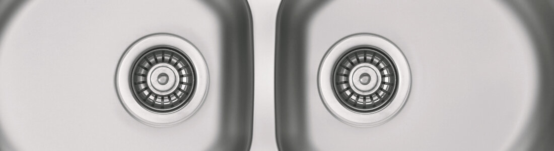 Zdjęcie przedstawia zlewozmywak dwukomorowy z widocznymi odpływami w każdej komorze. Powierzchnia jest metaliczna i ma satynowe wykończenie.