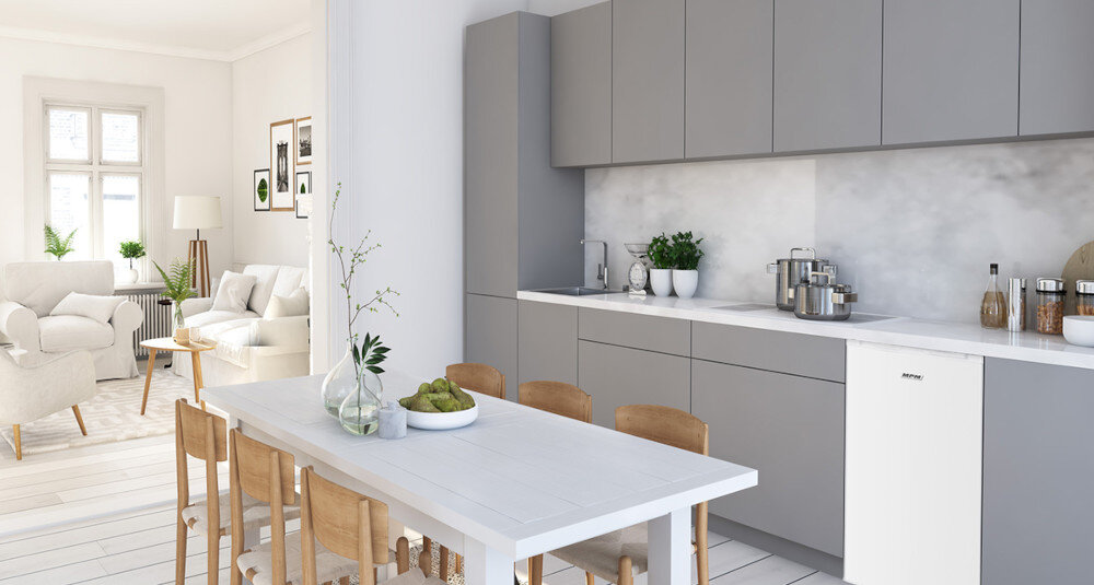 Nowoczesna kuchnia z szarymi szafkami i białym stołem, na którym stoi wazon z gałązkami i miska z owocami. W zabudowie kuchennej znajduje się zamrażarka z widocznym logo \'MPM\'.