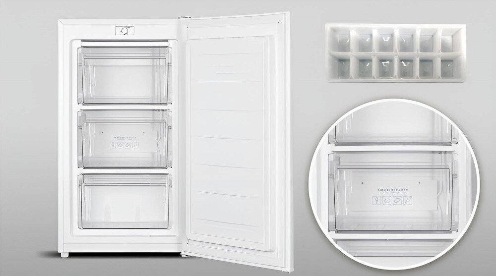 Otwarta biała zamrażarka z trzema przezroczystymi szufladami, na jednej z nich widoczny napis \'FROZEN ZONE\'. Obok zamrażarki znajduje się tacka na kostki lodu z kilkunastoma przegródkami.