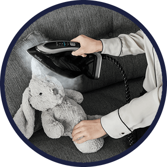 Osoba używa generatora pary do prasowania pluszowego królika na szarej kanapie. Urządzenie emituje parę, a na jego powierzchni widoczne jest logo TEFAL.