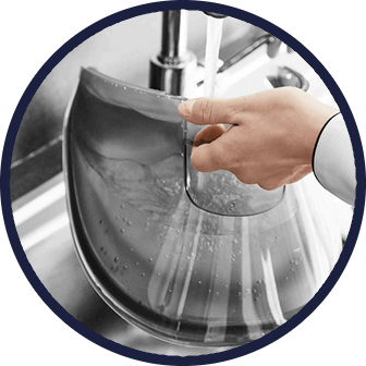 Osoba napełnia wodą przezroczysty pojemnik pod kranem. W tle widoczny jest zlew i strumień wody.