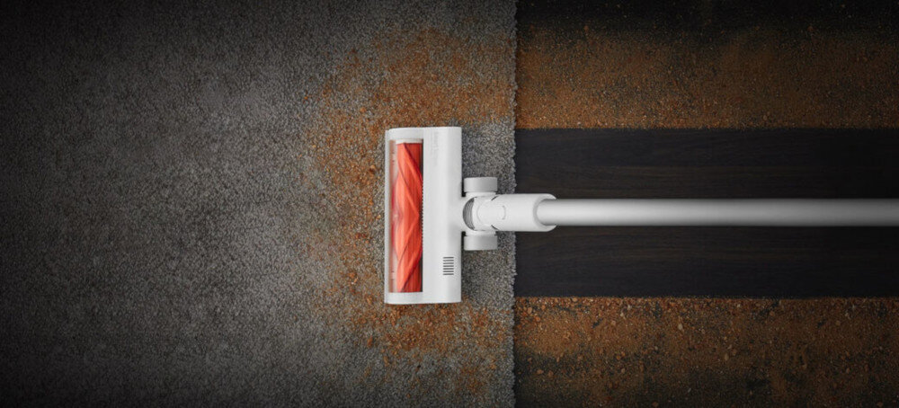 Na obrazie widoczna jest głowica odkurzacza z czerwonym wałkiem, która przesuwa się po powierzchni, czyszcząc ją z kurzu i brudu. Po jednej stronie powierzchnia jest czysta, a po drugiej pokryta kurzem.