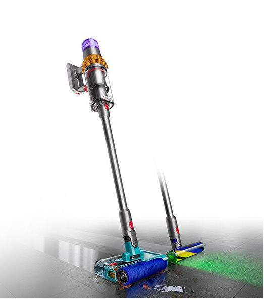 Na obrazie widoczny jest odkurzacz pionowy z funkcją aktywnego mycia, z kolorowymi elementami na głowicy czyszczącej. Urządzenie stoi na podłodze, na której widać ślady wody i zielone światło wskazujące na funkcję wykrywania zanieczyszczeń.