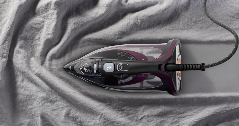 Żelazko w kolorze czarnym z fioletowymi elementami leży na szarej tkaninie. Na żelazku widoczne są przyciski i pokrętło regulacji pary.