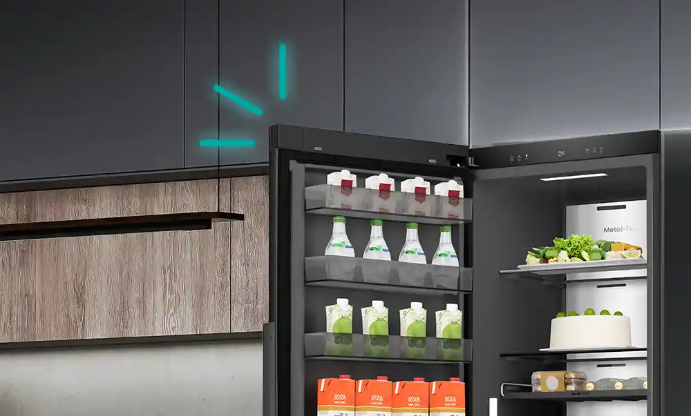 Otwarta czarna lodówka z widocznymi półkami, na których znajdują się kartony z napojami, butelki oraz warzywa. Wnętrze lodówki jest ciemne, a na tylnej ścianie widoczny jest napis \'Metal-Tech\'.