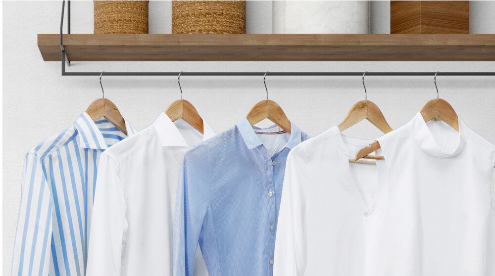 Na obrazie widoczne są cztery koszule wiszące na drewnianych wieszakach. W tle znajduje się półka z trzema koszami i drewnianym pudełkiem.