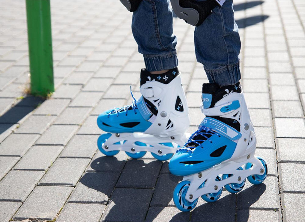 Osoba nosi niebiesko-białe łyżworolki na chodniku z kostki brukowej. Na łyżworolkach widoczne jest logo \'ENERO\'.