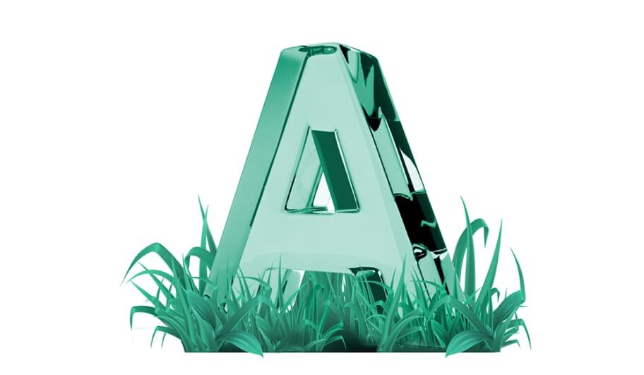 Szklana litera \'A\' w kolorze zielonym stoi wśród trawy.