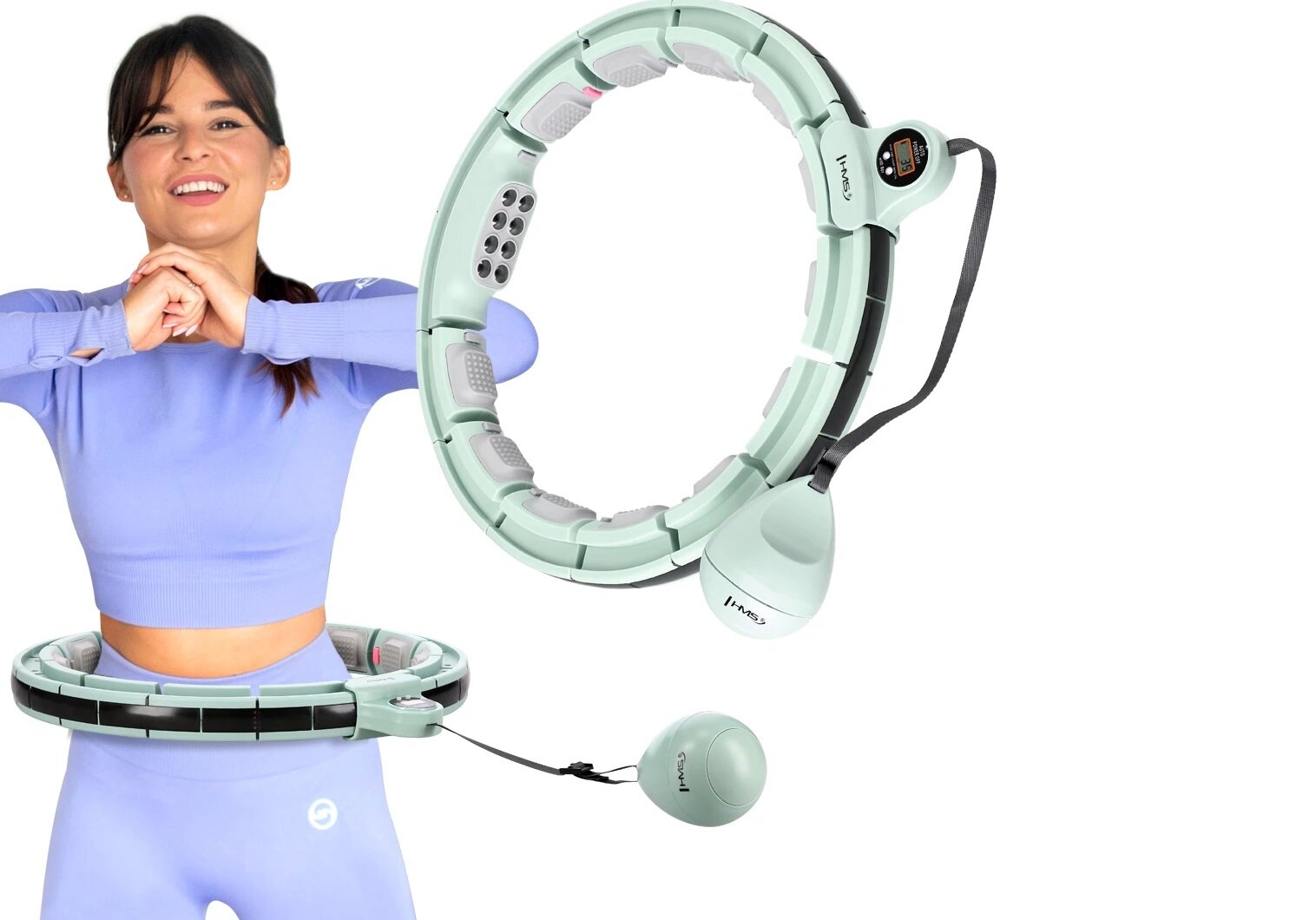 Osoba w niebieskim stroju trzyma ręce przed sobą, a wokół jej talii znajduje się zielone hula hop z dodatkowymi elementami. Na hula hop widoczne jest logo \'HMS\'.