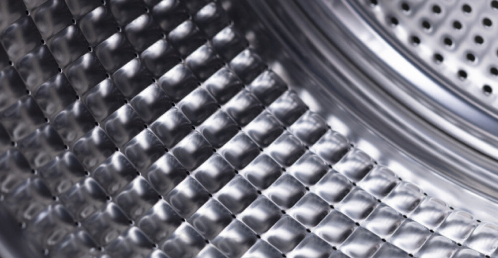 Zbliżenie na wnętrze bębna pralko-suszarki z metaliczną, perforowaną powierzchnią o wzorze przypominającym diamenty.