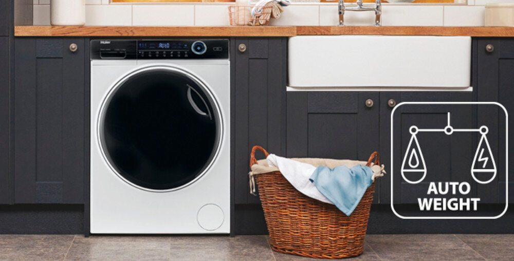 Pralko-suszarka w zabudowie kuchennej z widocznym panelem sterowania i dużym czarnym bębnem. Obok znajduje się kosz na pranie, a na obrazie widoczna jest ikona z napisem \'AUTO WEIGHT\'.