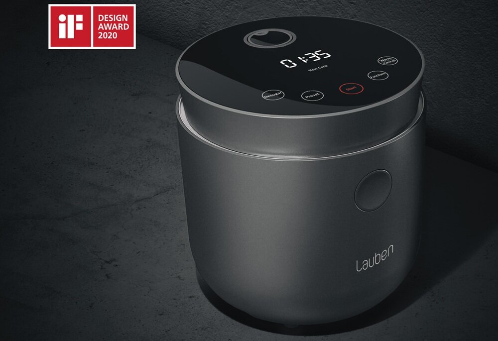 Na obrazie widoczny jest ryżowar o nowoczesnym designie z wyświetlaczem pokazującym czas 01:35 i przyciskami dotykowymi. W lewym górnym rogu znajduje się logo \'iF DESIGN AWARD 2020\'.