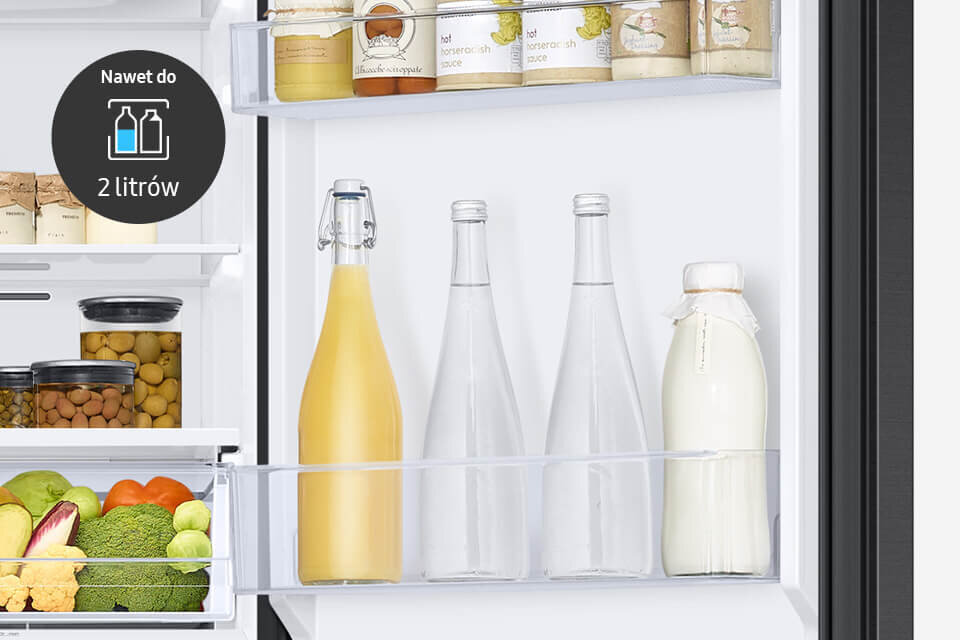 Wnętrze lodówki z widocznymi półkami, na których znajdują się słoiki, butelki i warzywa. Na drzwiach lodówki widoczna jest grafika z napisem \'Nawet do 2 litrów\'.