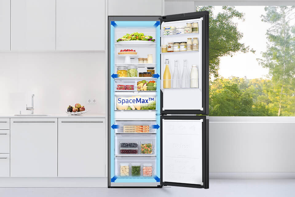 Otwarta lodówka z widocznymi półkami wypełnionymi różnymi produktami spożywczymi, na jednej z półek napis \'SpaceMax™\'. W tle jasna kuchnia z widokiem na zieleń za oknem.