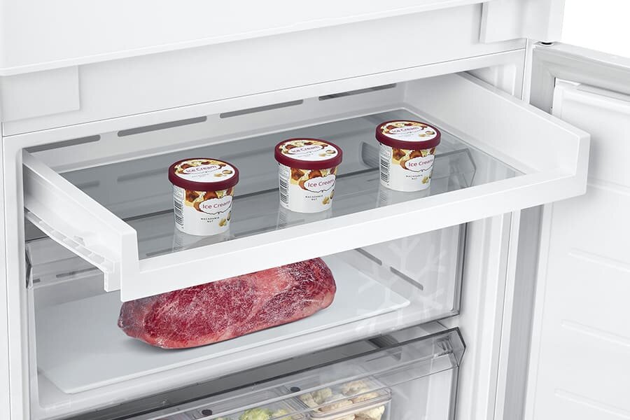 Dodatkowe cechy: Półka Easy Slide - Samsung lodówka z zamrażalnikiem BRB38G705DWW Wnętrze lodówki z wysuwaną półką, na której znajdują się trzy kubki lodów z napisem \'Ice Cream\'. Poniżej na półce leży duży kawałek mięsa na białej tacy.
