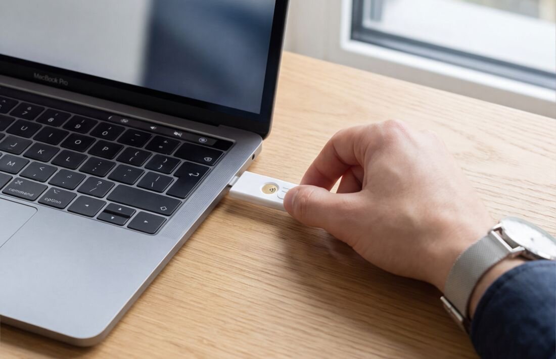 Użytkownik dotyka klucza zabezpieczającego HIRSCH Secure podłączonego do laptopa podczas bezpiecznego logowania w biurze 