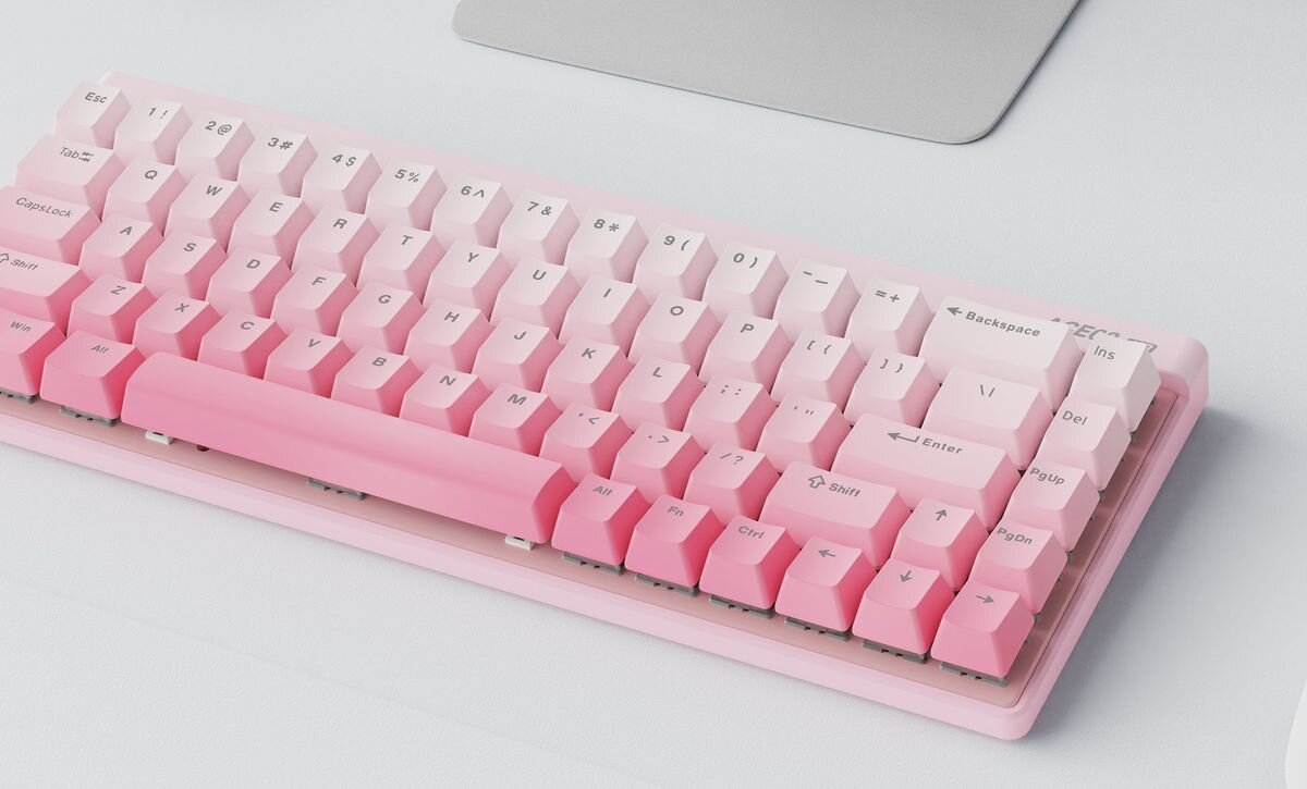 Klawiatura mechaniczna w kolorze różowym z białymi klawiszami, posiadająca układ QWERTY. Widoczne są klawisze z oznaczeniami liter, cyfr oraz funkcji takich jak \'Enter\', \'Shift\', \'Backspace\'.