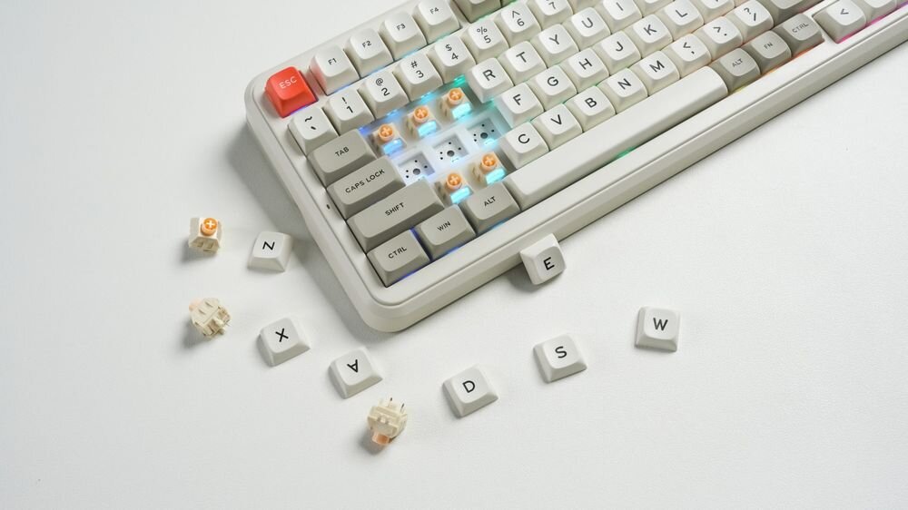 Na białym tle znajduje się klawiatura z retro klawiszami, z kilkoma zdjętymi klawiszami obok. Widoczne są klawisze z literami N, X, A, P, D, S, E, W oraz podświetlenie RGB pod niektórymi klawiszami.