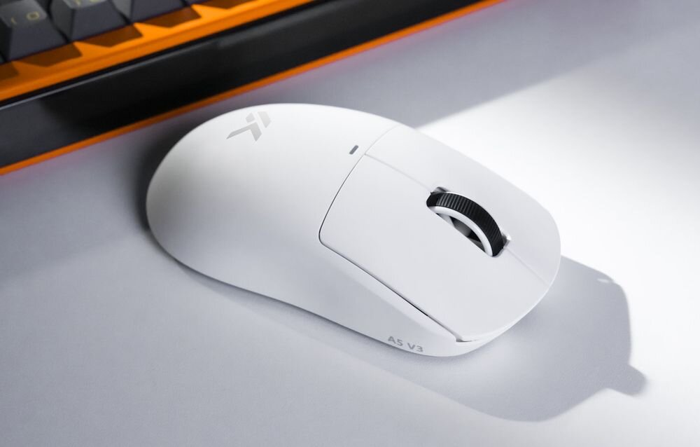 Mysz MCHOSE A5 V3 Ultra MCHOSE A5 V3 Ultra przewodową, 2.4 GHz oraz Bluetooth trybie 8K Polling Ready 8000 Hz przewodowo, jak i przez 2.4 GHz 8 razy więcej niż 1000 Hz - mysz pod skosem obok klawiatury na jasnym blacie