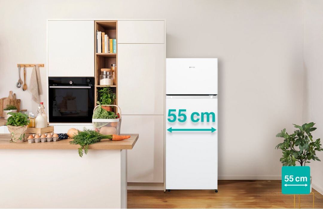 Biała lodówka z logo Gorenje stoi obok zabudowy kuchennej. Na lodówce widoczny jest napis \'55 cm\'.
