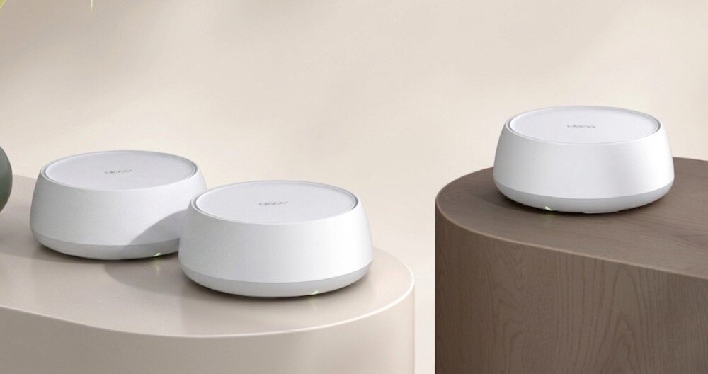 Router TP-LINK Deco BE22 Trzy okrągłe urządzenia sieciowe ustawione na dwóch nowoczesnych stolikach w jasnym wnętrzu, opis