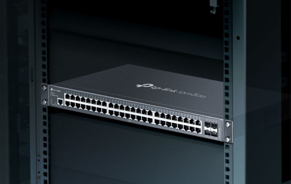 Switch TP-LINK Omada SG3452X Przełącznik sieciowy zamontowany w ciemnej metalowej szafie serwerowej Rack widoczny od przodu w oświetleniu punktowym, opis