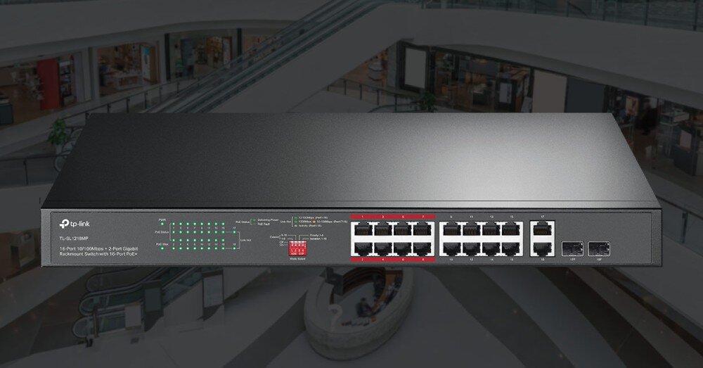 Switch TP-LINK TL-SL1218MP V2 Przedni panel przełącznika sieciowego z widocznymi portami RJ45 i diodami sygnalizacyjnymi, zaprezentowany na rozmytym tle wnętrza galerii handlowej, opis