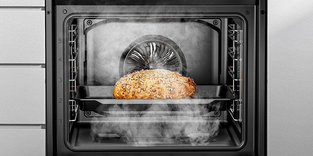 Wnętrze piekarnika z piekącym się chlebem na blasze, otoczone parą. W tle widoczny wentylator termoobiegu.