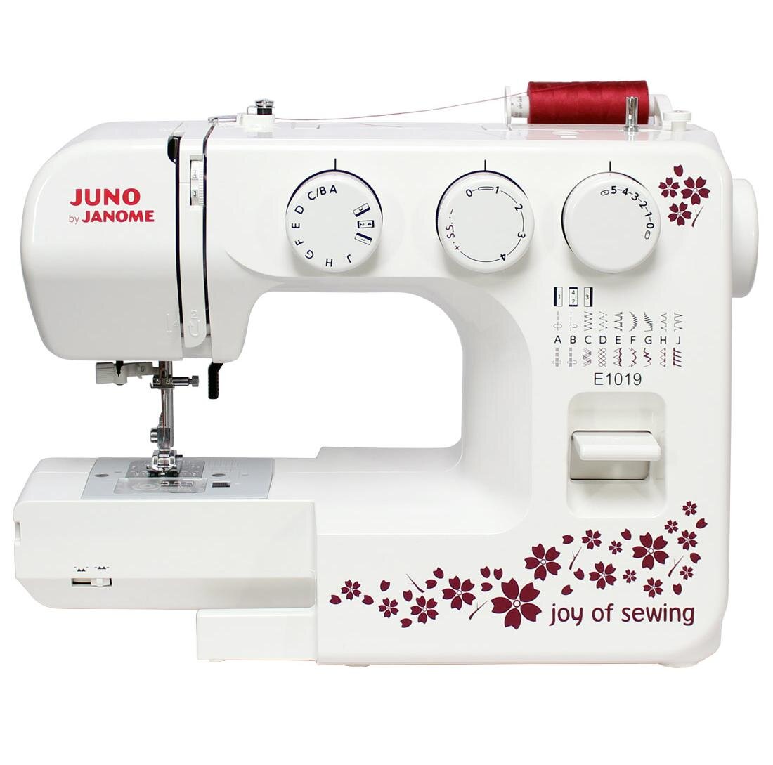 Biała maszyna do szycia z czerwonymi kwiatowymi wzorami i napisem \'joy of sewing\'. Widoczne są pokrętła z oznaczeniami literowymi i numerycznymi oraz napis \'JUNO by JANOME\'.
