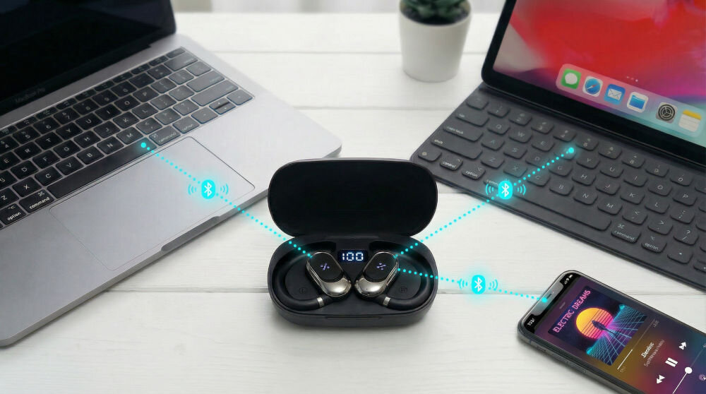 Słuchawki powietrzne XMUSIC XWS550K Widok z góry na jasne, drewniane biurko. Pośrodku otwarte czarne etui ładujące ze słuchawkami bezprzewodowymi. Na ekranie wskaźnik 100%. Po lewej stronie otwarty laptop, po prawej tablet z klawiaturą oraz smartfon z włączoną aplikacją muzyczną ELECTRIC DREAMS. Niebieskie, przerywane linie ze świecącymi ikonami Bluetooth łączą etui ze wszystkimi trzema urządzeniami, ilustrując połączenie. W tle mała roślina doniczkowa.