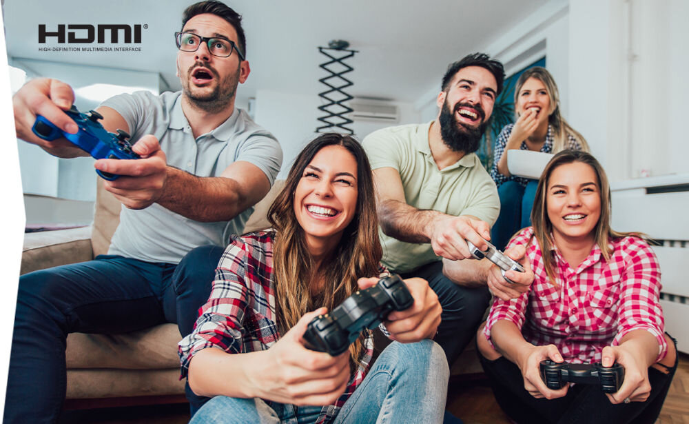 Grupa pięciu osób siedzi na kanapie, trzymając kontrolery do gier i patrząc w stronę ekranu. W lewym górnym rogu widoczne jest logo HDMI z napisem \'High Definition Multimedia Interface\'.