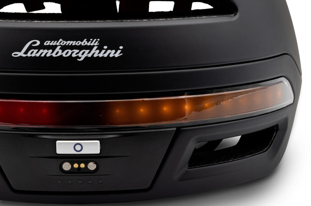 Czarny kask z widocznym logo \'automobili Lamborghini\' oraz pomarańczowym paskiem świetlnym. Na dole znajduje się przycisk z niebieskim okręgiem i trzy złote styki.