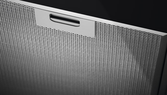 Zbliżenie na metalowy filtr okapu z uchwytem na górze. Filtr ma drobną siateczkową strukturę.