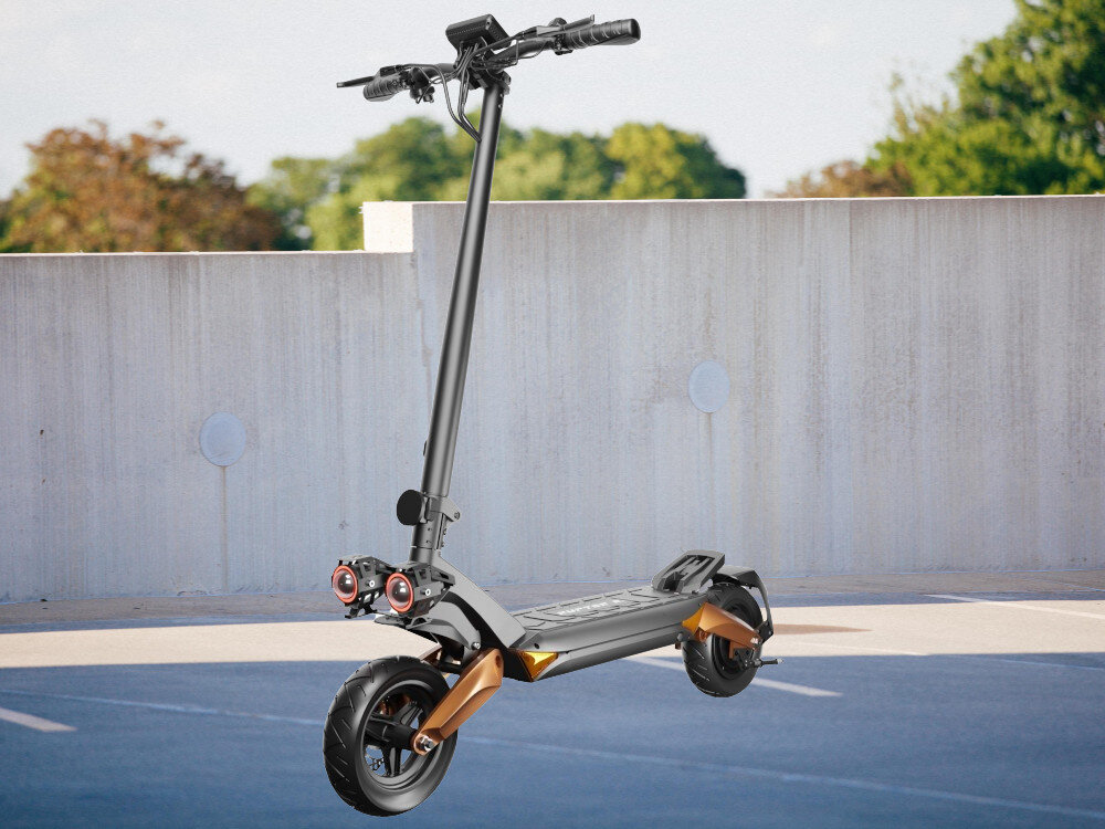 Hulajnoga elektryczna z dużymi kołami i miedzianymi elementami zawieszenia stoi na tle betonowej ściany. W tle widoczne są drzewa i niebo.