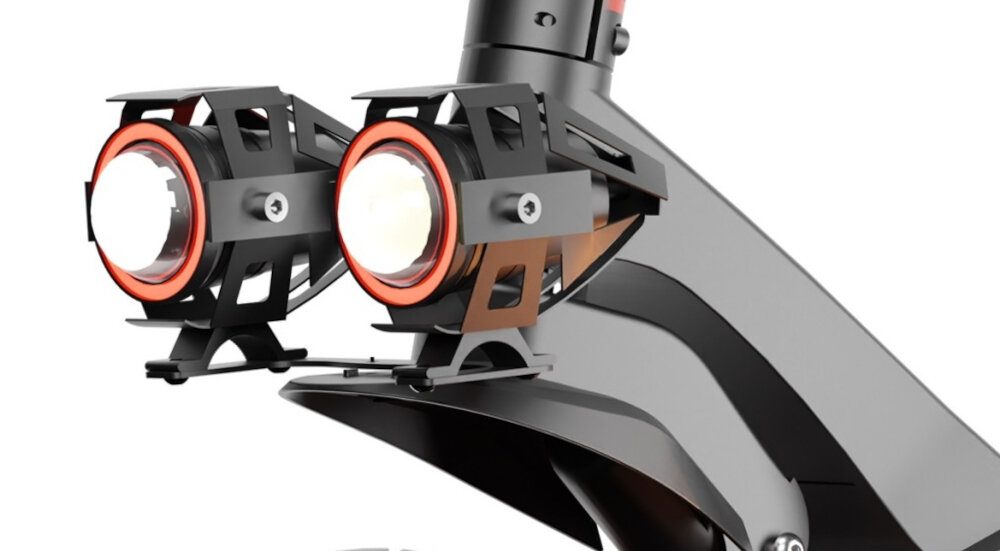 Zbliżenie na dwa reflektory zamontowane na metalowej konstrukcji, z widocznymi pomarańczowymi akcentami. Reflektory są częścią większego urządzenia o nowoczesnym designie.