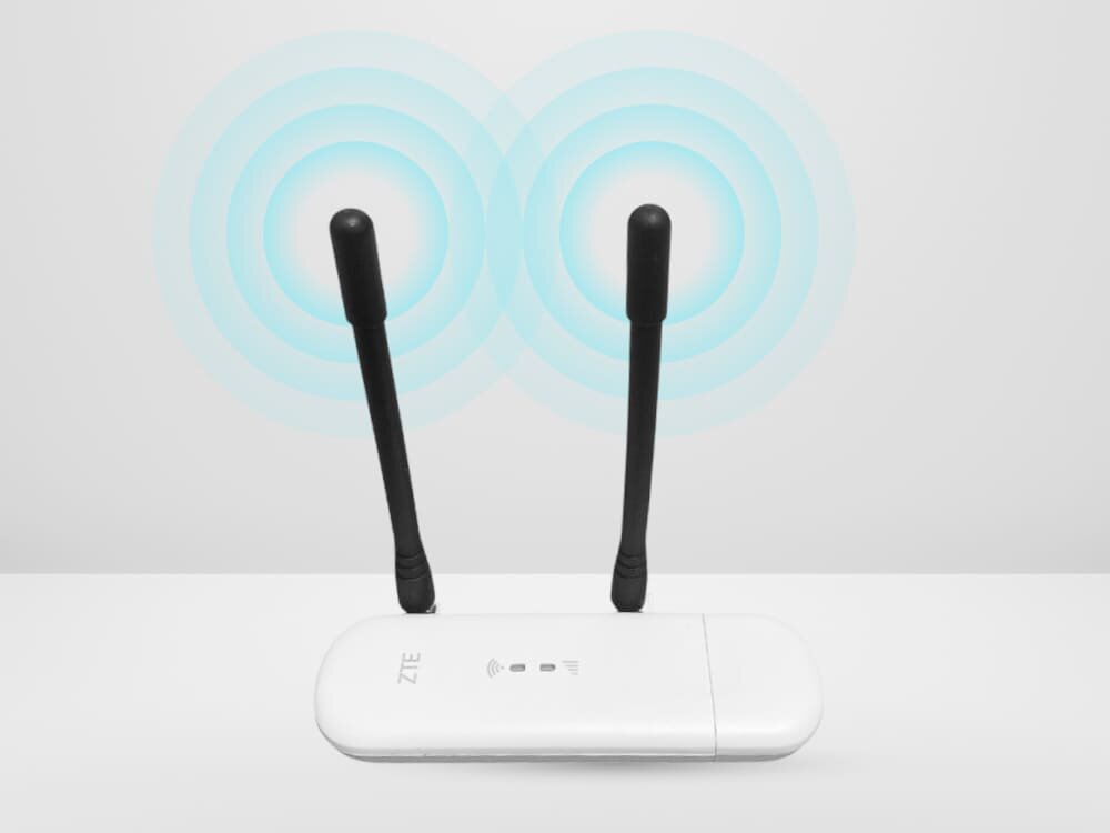Modem ZTE MF79N 4G LTE Biały modem ZTE z dwiema czarnymi antenami emituje niebieskie fale sygnału. Obraz podkreśla możliwość podłączenia zewnętrznych anten TS9 dla lepszej jakości sygnału LTE, złącza antenowe, sygnał