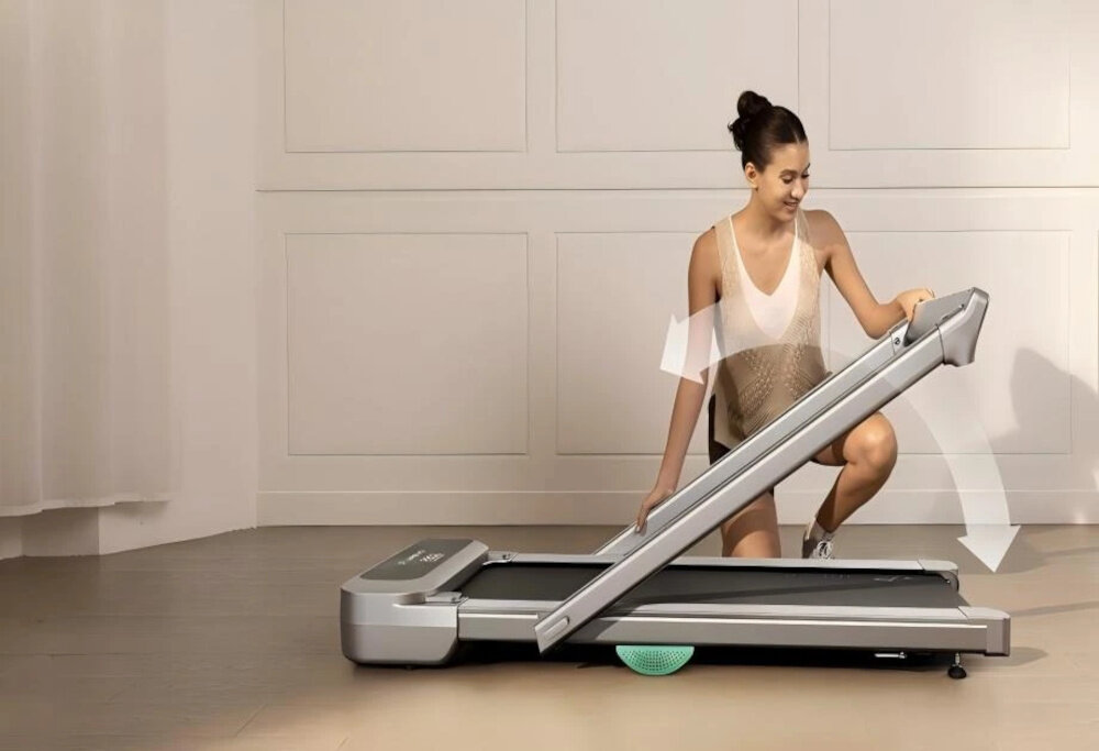 Bieżnia elektryczna UREVO Foldmix 5L Pro 2237W 13.4 km-h pokój osoba składa bieżnię strzałka pokazująca możliwość złożenia w tle biała ściana bieżnię można złożyć do wymiarów 70 x 14 x 158 cm rolki transportowe składana konstrukcja