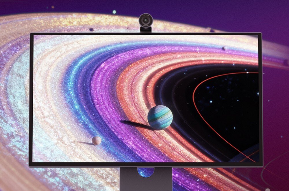Monitor wyświetla kolorową grafikę przedstawiającą pierścienie planety z widocznymi planetami w tle. Na górze monitora znajduje się kamera.