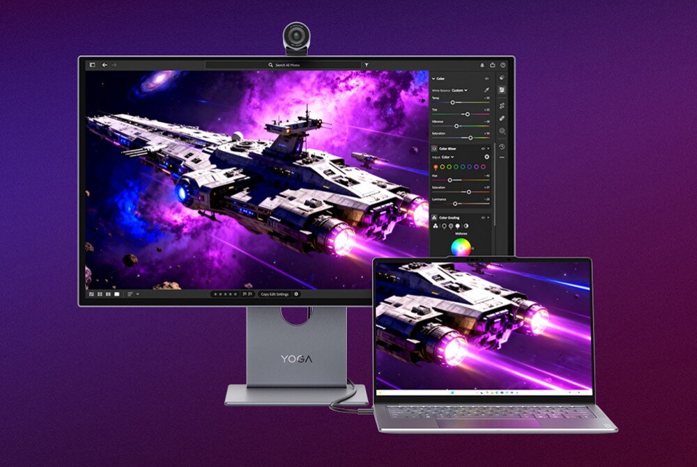 Na obrazie widoczny jest monitor z logo \'YOGA\' oraz laptop, oba wyświetlają grafikę przedstawiającą statek kosmiczny na tle fioletowej przestrzeni kosmicznej. Monitor posiada kamerę na górze ekranu.