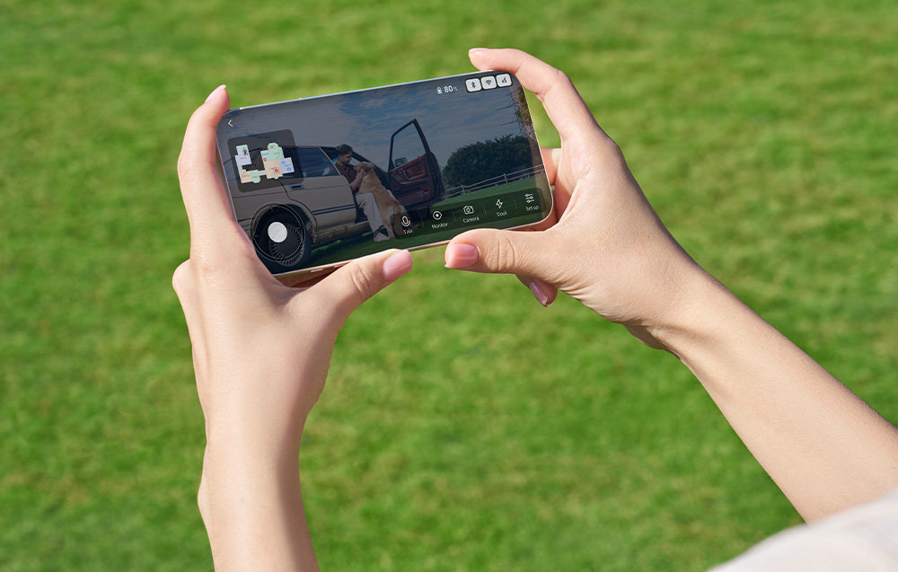 Robot koszący DREAME A3 AWD 1600 bez przewodu ograniczającego trawnik osoba trzyma telefon w dłoni z widokiem na drugą osobę siedzącą w samochodzie i głaszczącą psa aplikacja mobilna Dreamehome można ustawić harmonogram wyznaczyć strefy kontrolować wydajność obsługiwać różne obszary funkcja Dual-Map dwie mapy wbudowany modułu Bluetooth poprzez sieć Wi-Fi