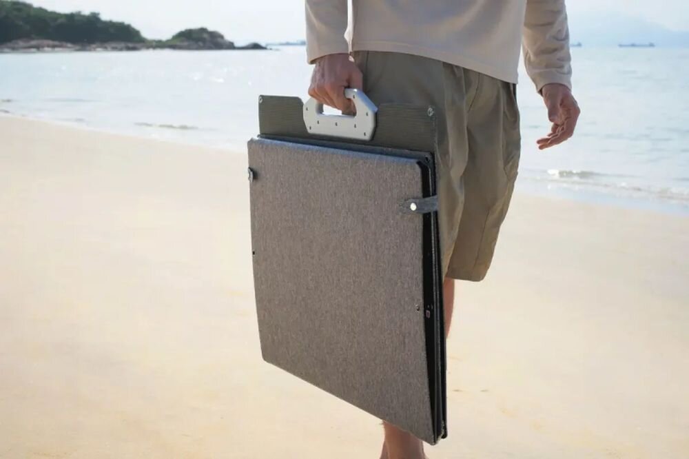 Panel fotowoltaiczny DJI POWER 200W, słońce, panel, energia, zasilanie, osoba niesie złożony panel przez słoneczną plażę