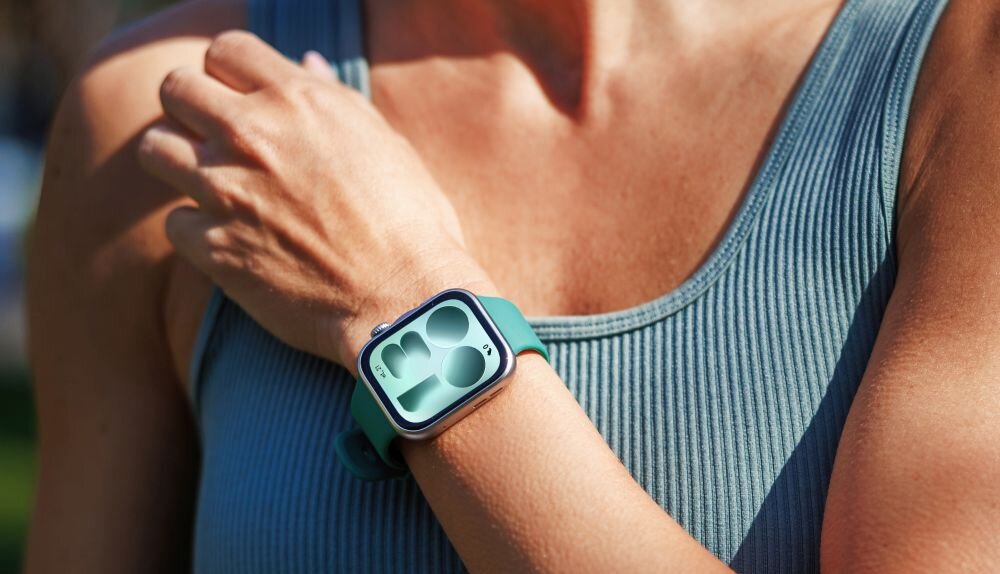 Osoba nosi smartwatch z zielonym paskiem na nadgarstku. Wyświetlacz zegarka pokazuje grafikę z trzema okręgami.