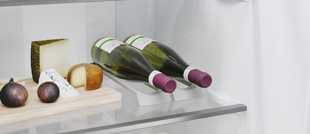 Wnętrze lodówki z dwoma butelkami wina leżącymi na półce oraz deską serów z dwoma figami. Butelki mają fioletowe korki, a na desce znajdują się różne rodzaje sera.
