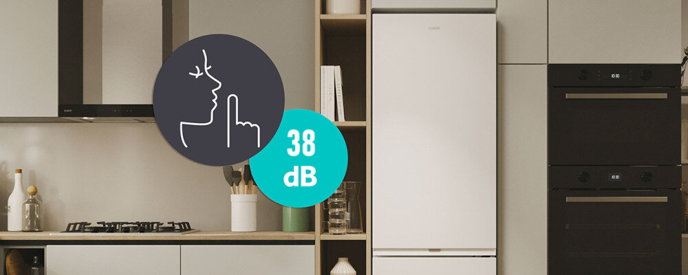 Kuchnia z białą lodówką w zabudowie, obok której znajduje się piekarnik i płyta grzewcza. Na obrazie widoczna jest ikona z symbolem ciszy i napisem \'38 dB\'.