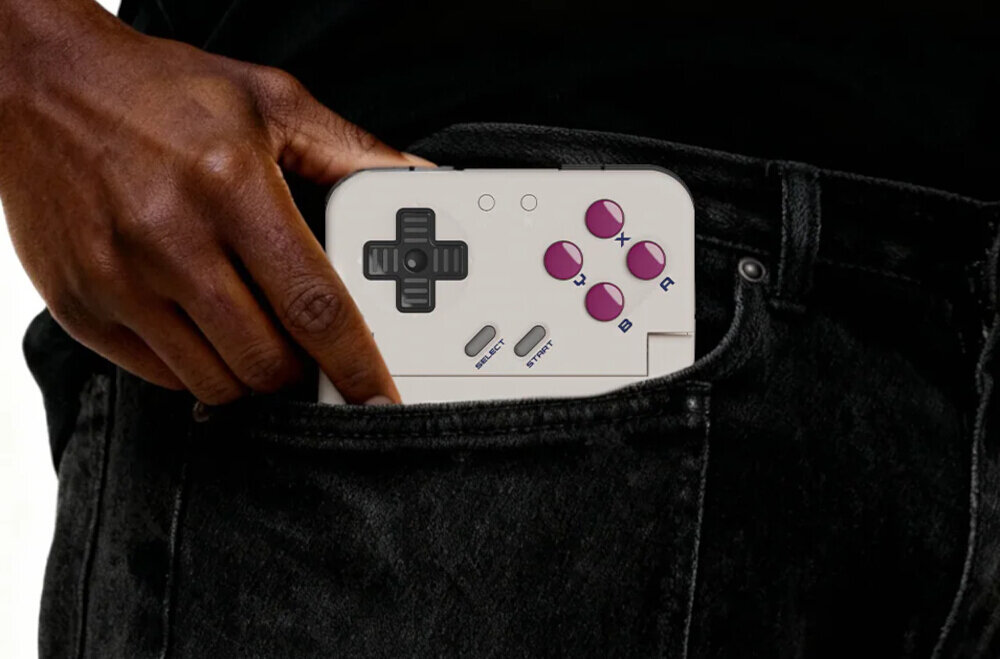 Osoba wkłada biały kontroler do kieszeni spodni. Kontroler ma przyciski w kolorze fioletowym oraz krzyżak kierunkowy.