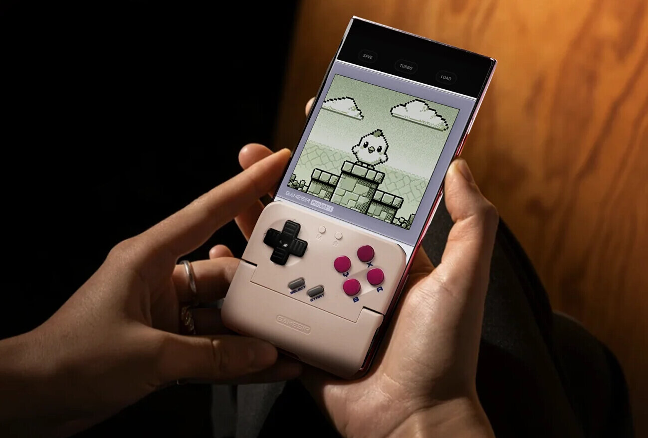 Osoba trzyma urządzenie przypominające konsolę do gier z ekranem wyświetlającym grafikę w stylu retro. Na urządzeniu widoczne są przyciski kierunkowe i funkcyjne oraz logo \'GAMESIR\'.