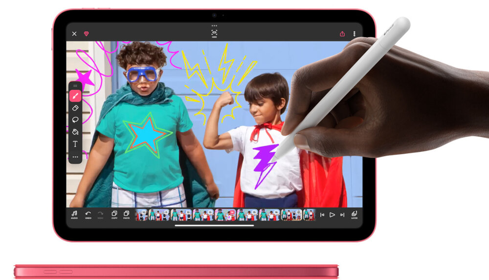 Tablet z ekranem dotykowym, na którym widać aplikację do edycji zdjęć z dwójką dzieci w kostiumach superbohaterów. Ręka trzymająca rysik rysuje na ekranie fioletowy błyskawicę na koszulce jednego z dzieci.