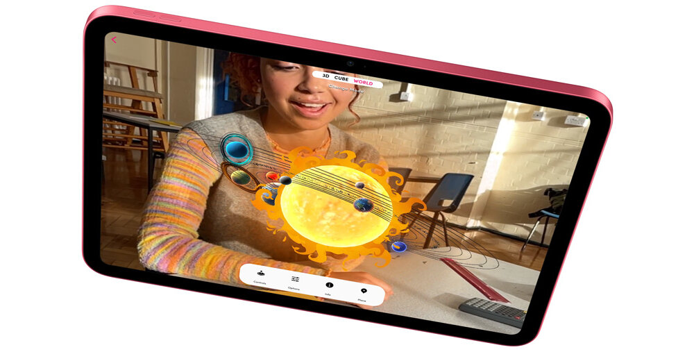 Tablet wyświetla aplikację z modelem układu słonecznego, na którym widoczna jest animacja słońca i planet. W tle znajduje się osoba w pomieszczeniu z drewnianymi meblami.